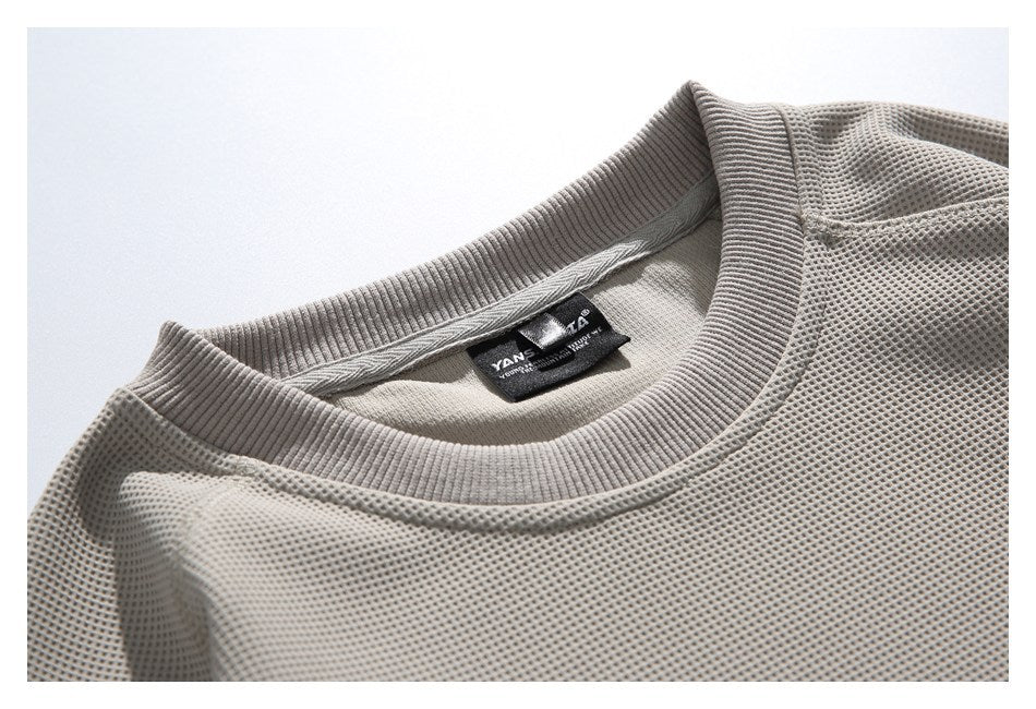 Close-up of a light gray waffle-textured sweatshirt neckline, ribbed collar, and sewn-in label.