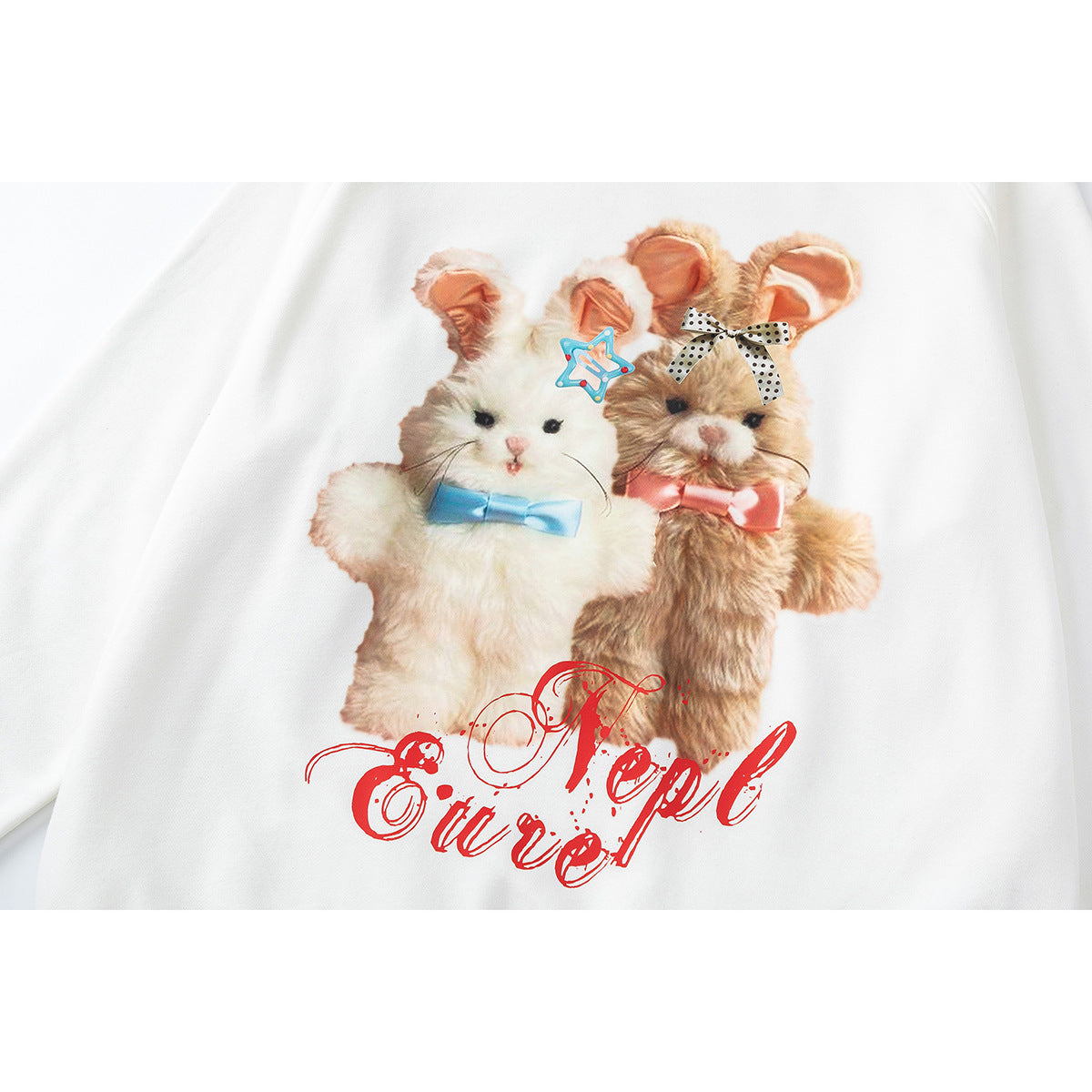 Close-up of a white sweatshirt printed with two fluffy animals in bows and large red script lettering.