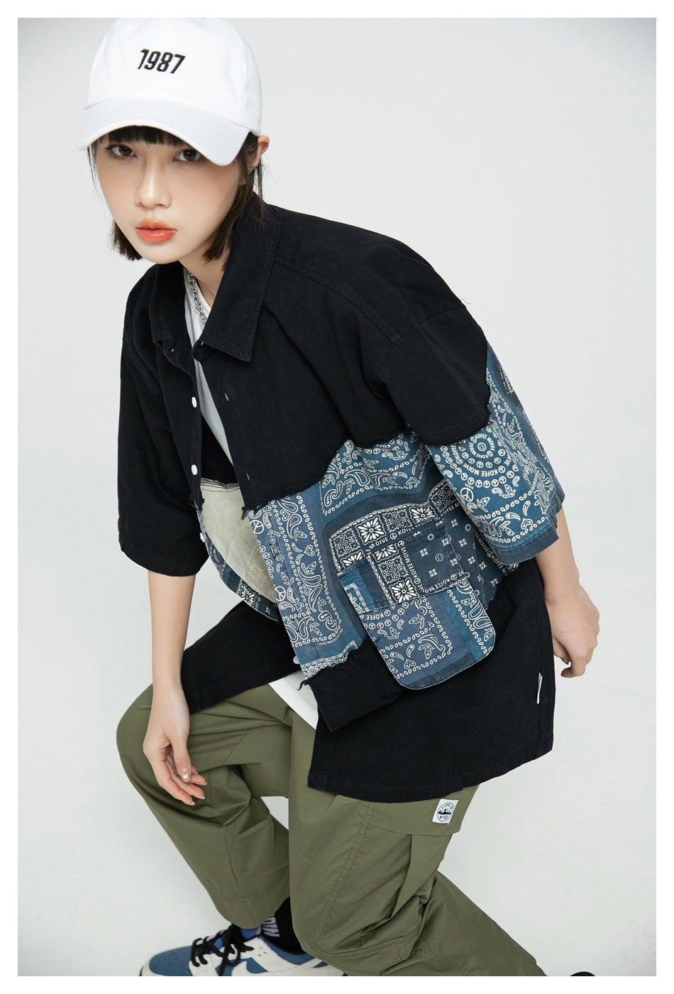 Close view of a model wearing an oversized black shirt with blue bandana-print panels and olive cargo pants.