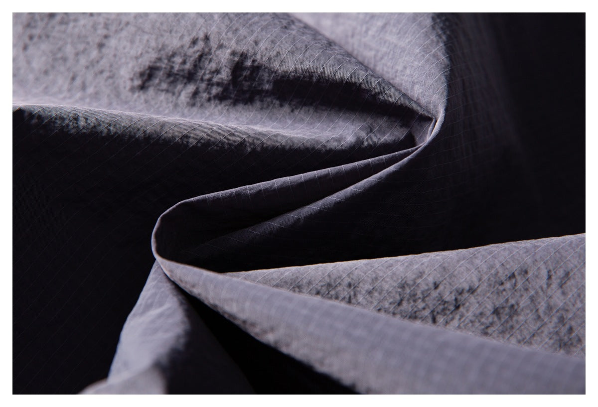 Close-up of folded dark gray ripstop fabric showing its fine grid texture and seams.