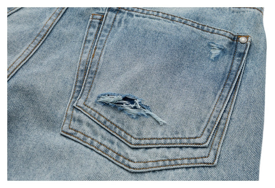 Close-up of a distressed rear pocket on light-wash jeans, with frayed rips and orange-brown stitching.