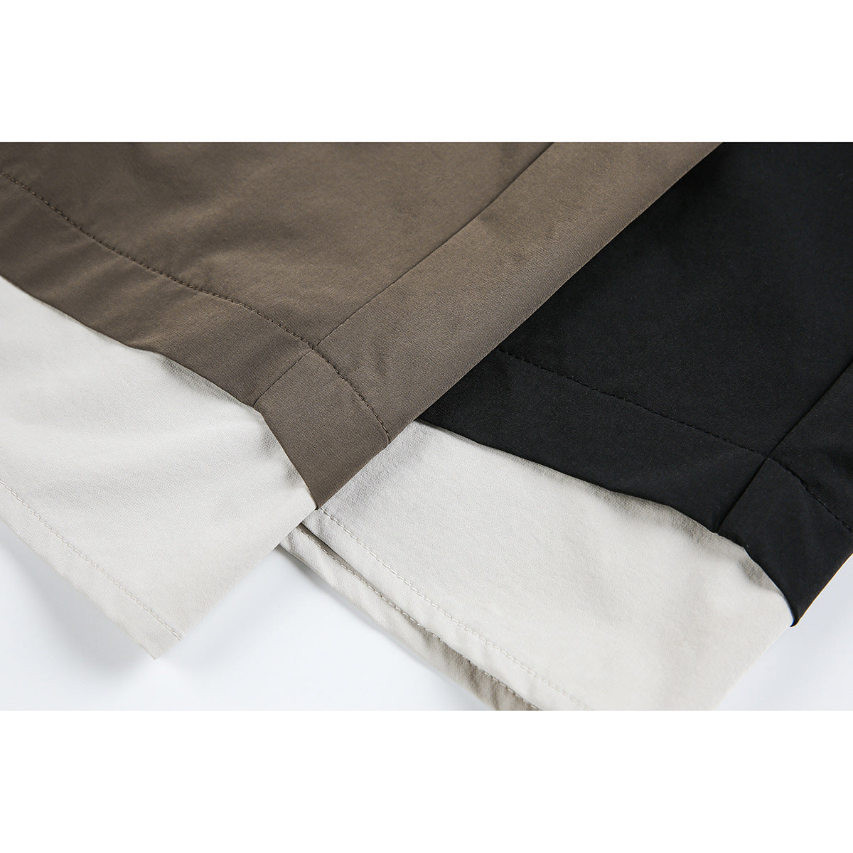 Close-up of overlapping taupe, black, and off-white shorts hems with visible stitching.