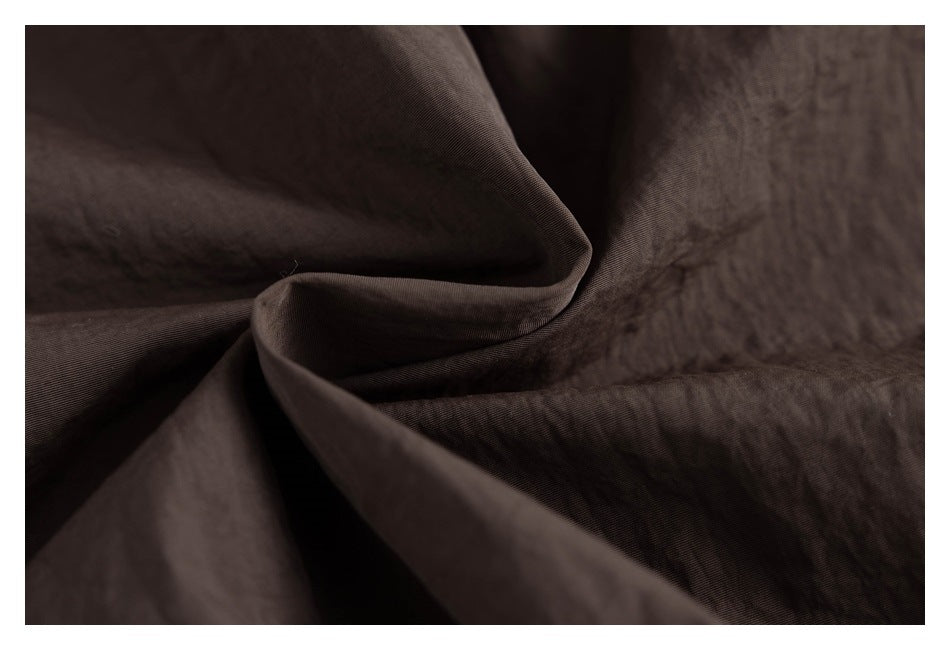 Close-up of dark brown fabric gathered into folds, showing a fine diagonal weave.