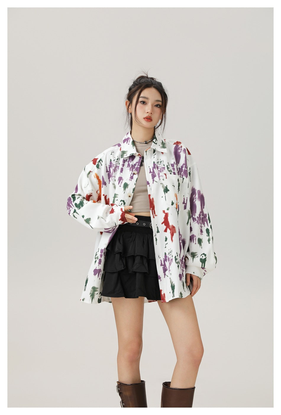 Model wearing an oversized white shirt with purple, green and red print over a beige top and black ruffle skirt