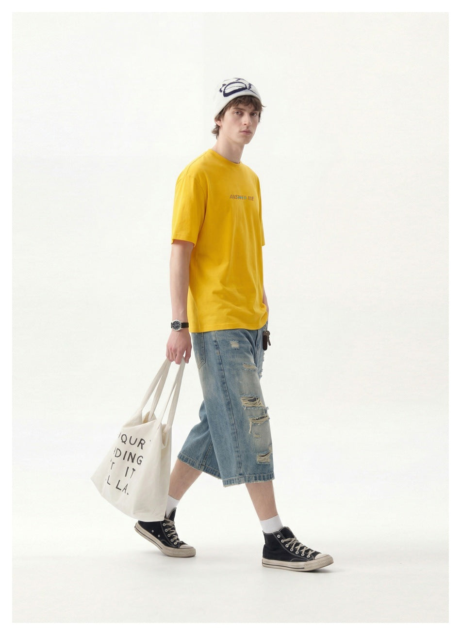 Side-angled view of a man in a yellow T-shirt walking with distressed denim shorts and a canvas tote bag