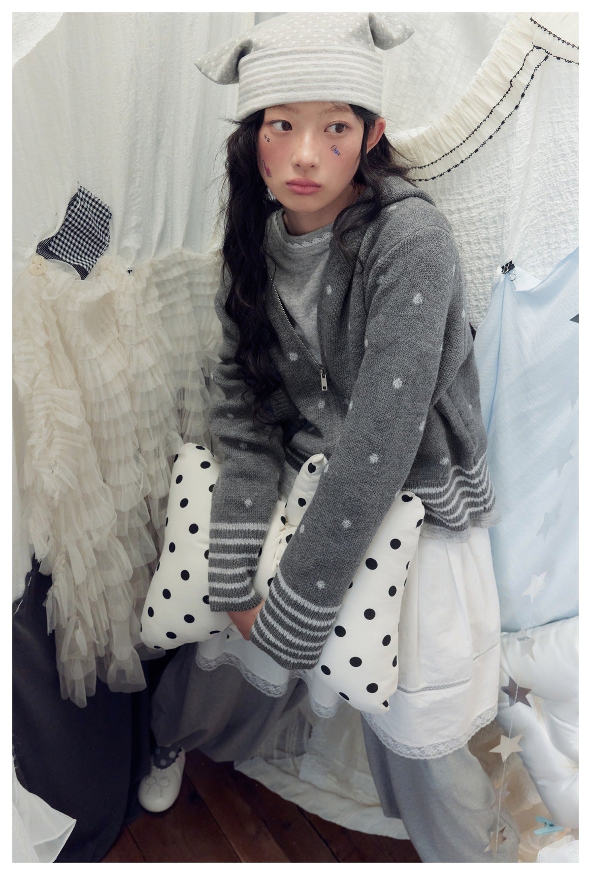Model wearing a gray hooded zip cardigan with small white dots and striped cuffs, layered over a gray top and white skirt.