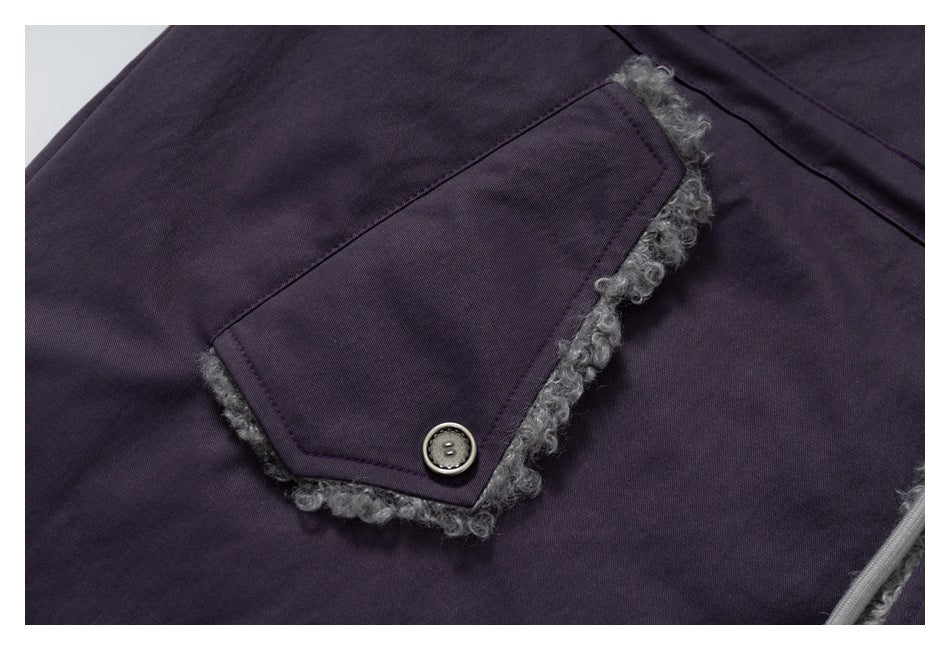 Close-up of a dark purple coat's buttoned flap pocket edged with gray fuzzy trim.