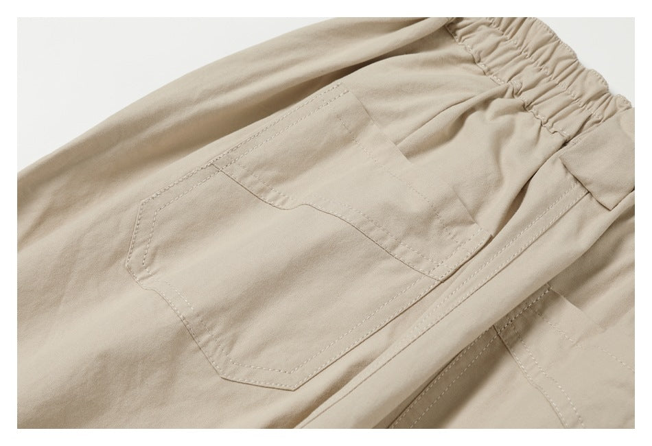 Close-up of a stitched patch pocket and elastic waistband on beige trousers.
