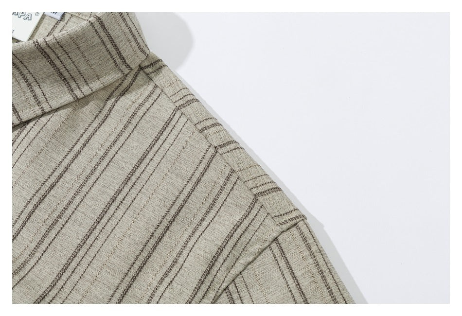 Close-up of a beige shirt collar and shoulder with thin dark stripes and a small partially visible tag.