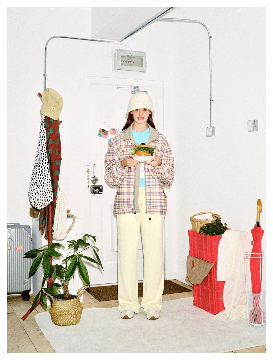 Front view of a model wearing a pastel plaid zip jacket with gray trim and cream pants, holding a plate of food.