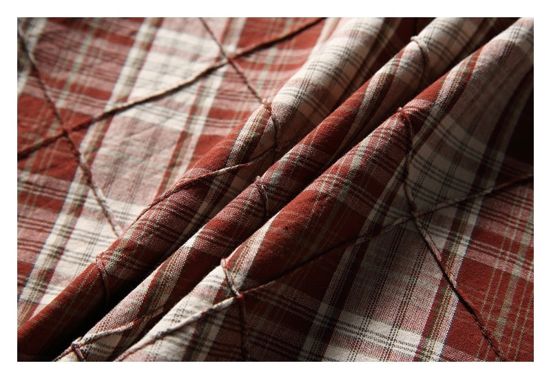 Close-up of reddish-brown, cream, and gray plaid fabric with raised diagonal stitched lines and folded layers.