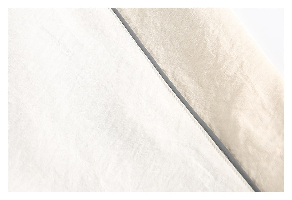 Close-up of cream jacket fabric with a diagonal gray piped seam.