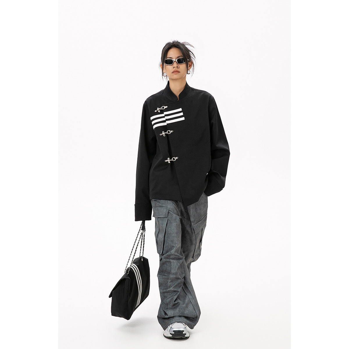 Full-length model wearing a black clasp-front jacket with white stripes and loose gray cargo pants.