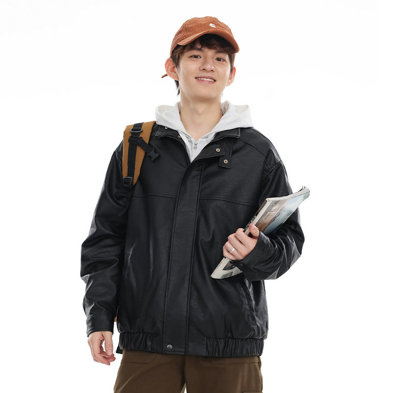 Model wearing a black stand-collar jacket with snap details and an elastic hem, carrying a shoulder bag and magazine.