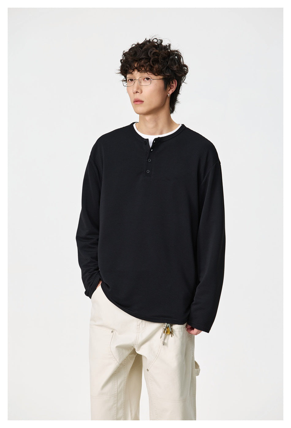 Model wearing a black ribbed long-sleeve henley and cream trousers, shown from the front at a slight angle.