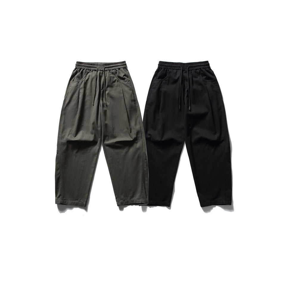 Two pairs of relaxed pants shown from the front, in dark olive and black, with elastic drawstring waists and pockets.