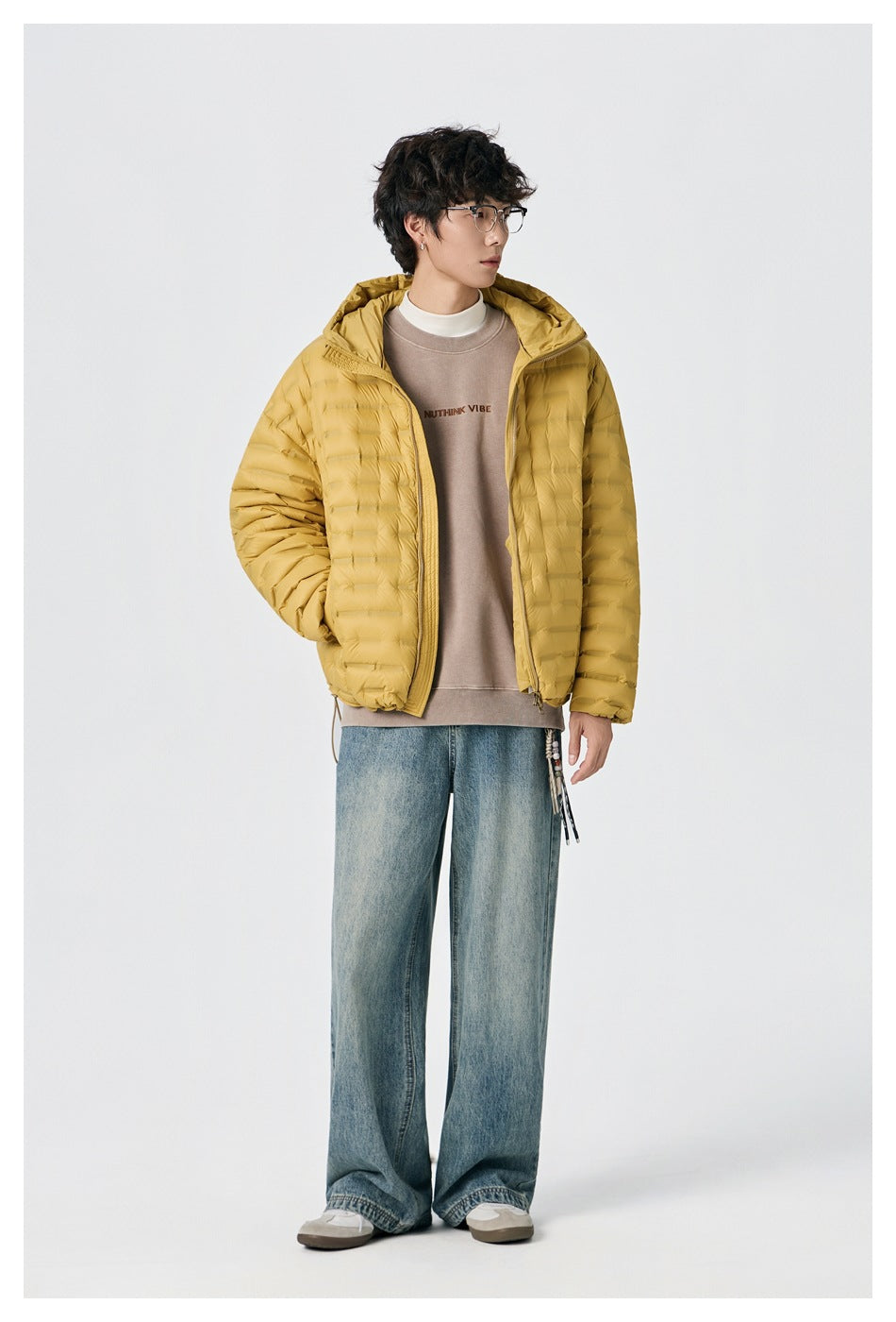 Full-length front view of a model wearing an open mustard-yellow hooded quilted jacket with jeans.