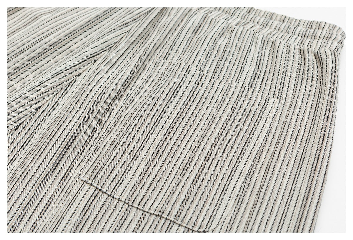 Close-up of a rectangular pocket on cream bottoms with narrow black and gray vertical stripes.