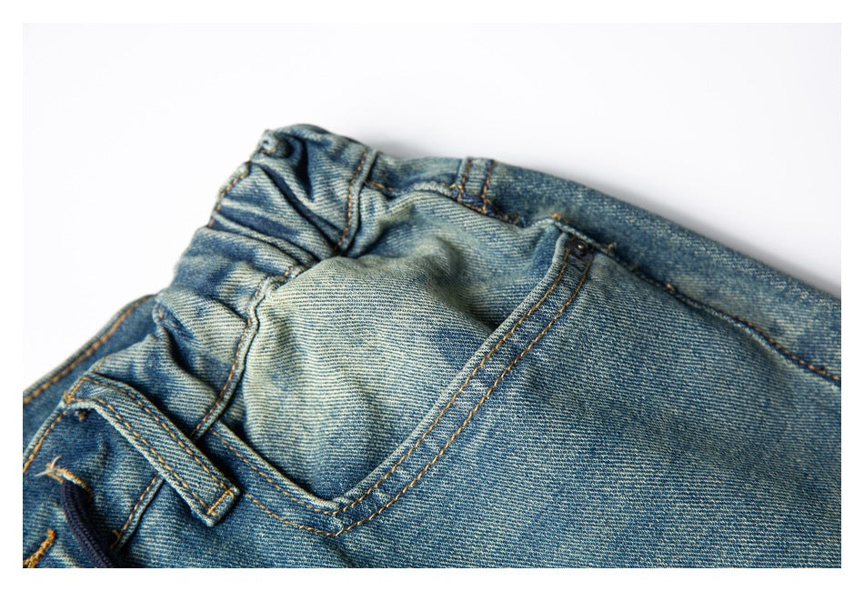 Close-up of the back pocket and elasticized waistband on faded blue denim trousers.