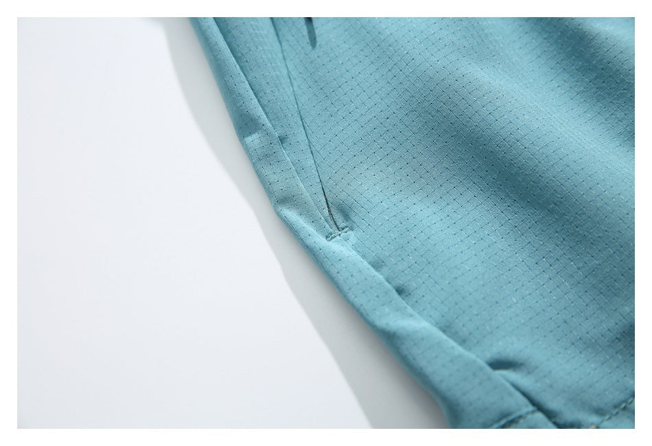 Close-up of light blue shorts showing a curved seam, hem stitching and subtle dotted fabric texture.