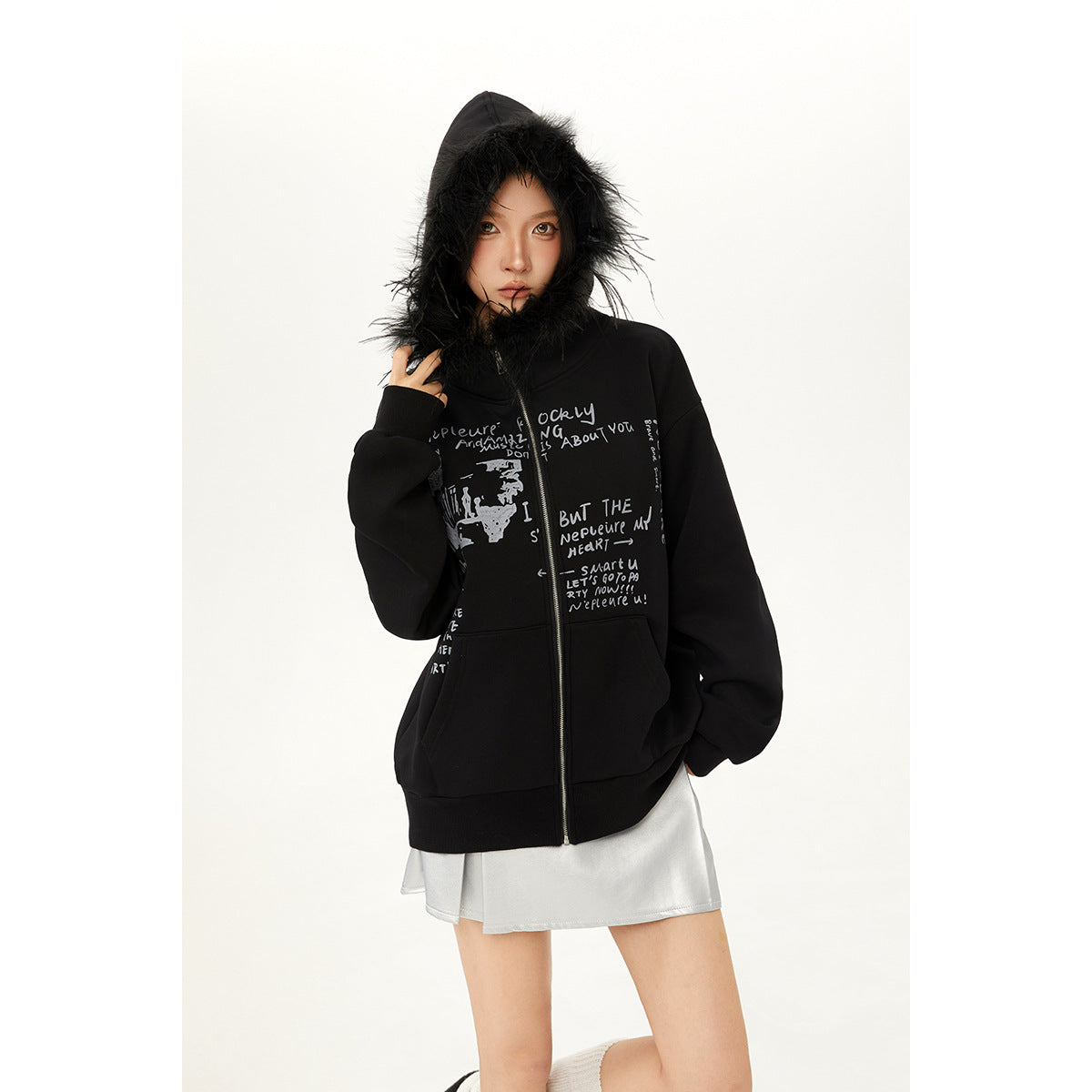 Model wearing a black graphic zip hoodie with its fur-trimmed hood up and a silver skirt.