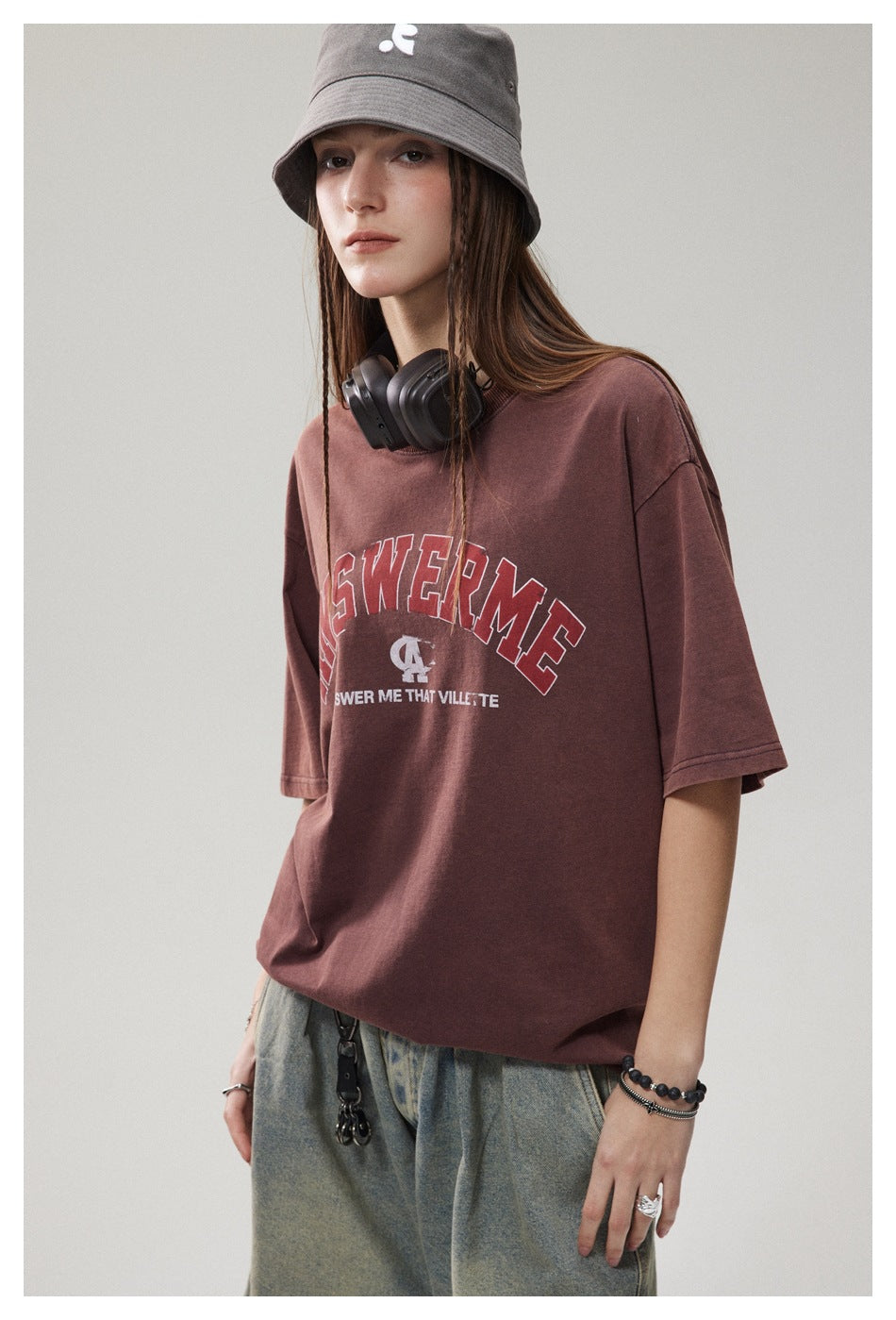 Model wearing an oversized burgundy graphic T-shirt with loose gray jeans and a gray bucket hat.