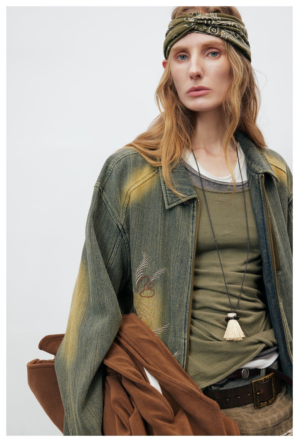Close-up of a model wearing an olive distressed embroidered jacket over layered tops, with a patterned headband.