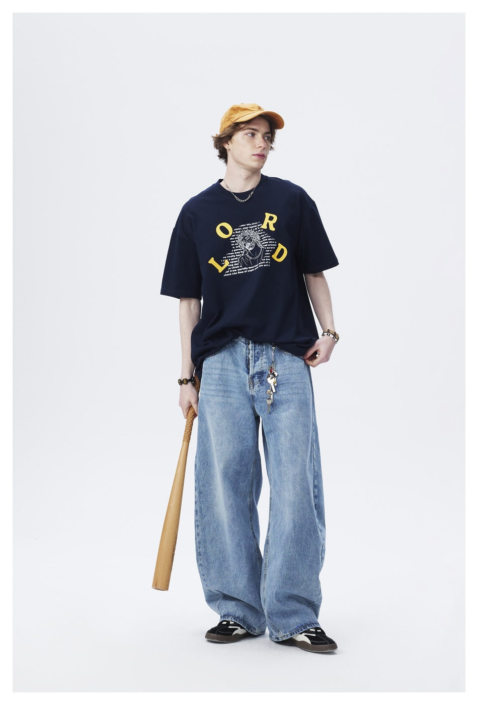 Model wears a navy graphic T-shirt and wide-leg light-blue jeans with a mustard cap.