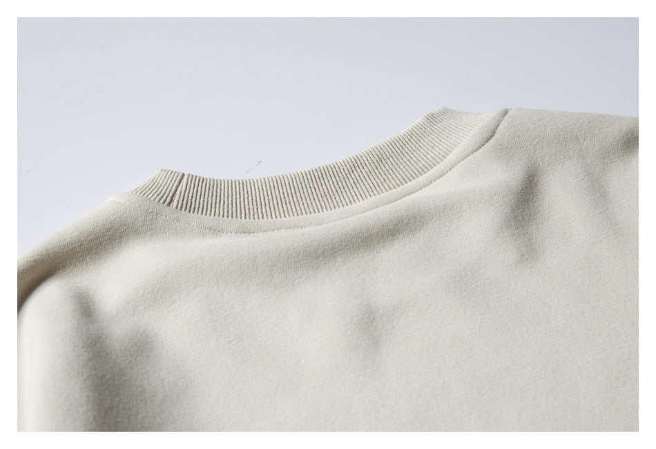 Close-up of a pale cream garment showing its ribbed crew neckline and shoulder seam.
