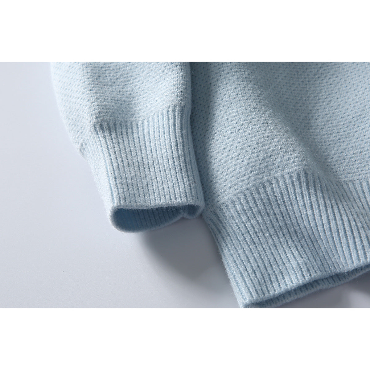 Close-up of a pale blue cardigan sleeve and body, highlighting the ribbed cuff and hem.