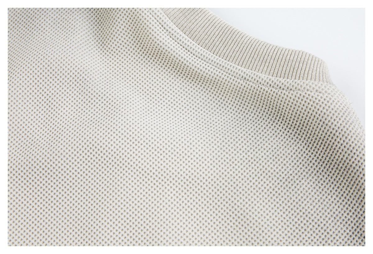 Close-up of an ivory waffle-knit garment's ribbed collar and shoulder seam.