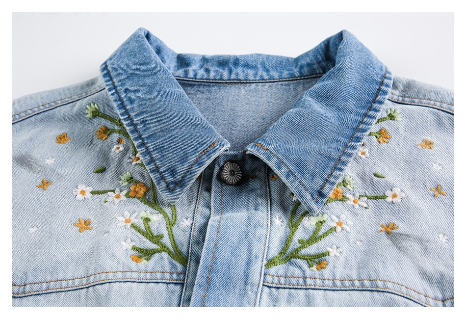 Close-up of a light blue jacket collar and chest with embroidered white and yellow flowers and green stems.