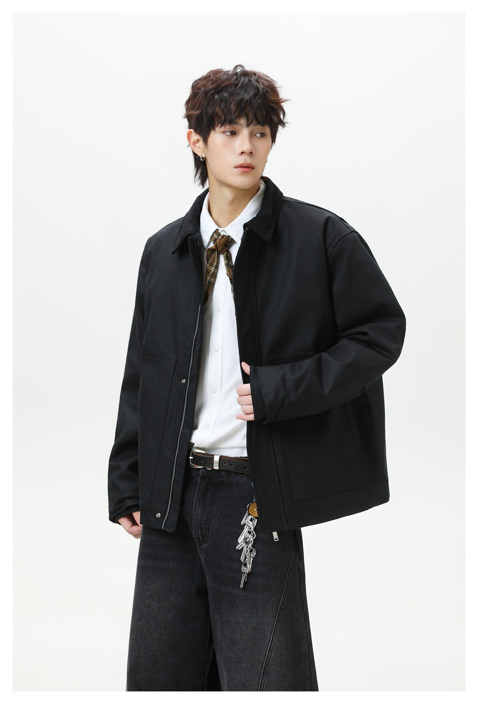 Model wearing a black zip-front jacket with a collar and large patch pockets, styled with a white shirt and plaid tie.