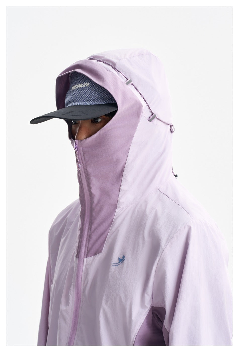 Close-up of a person wearing a pale lavender hooded jacket zipped over a dark cap, with the hood covering the lower face.