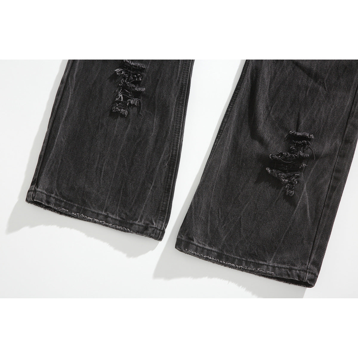Close-up of the lower legs of black washed jeans, with distressed patches and finished hems.