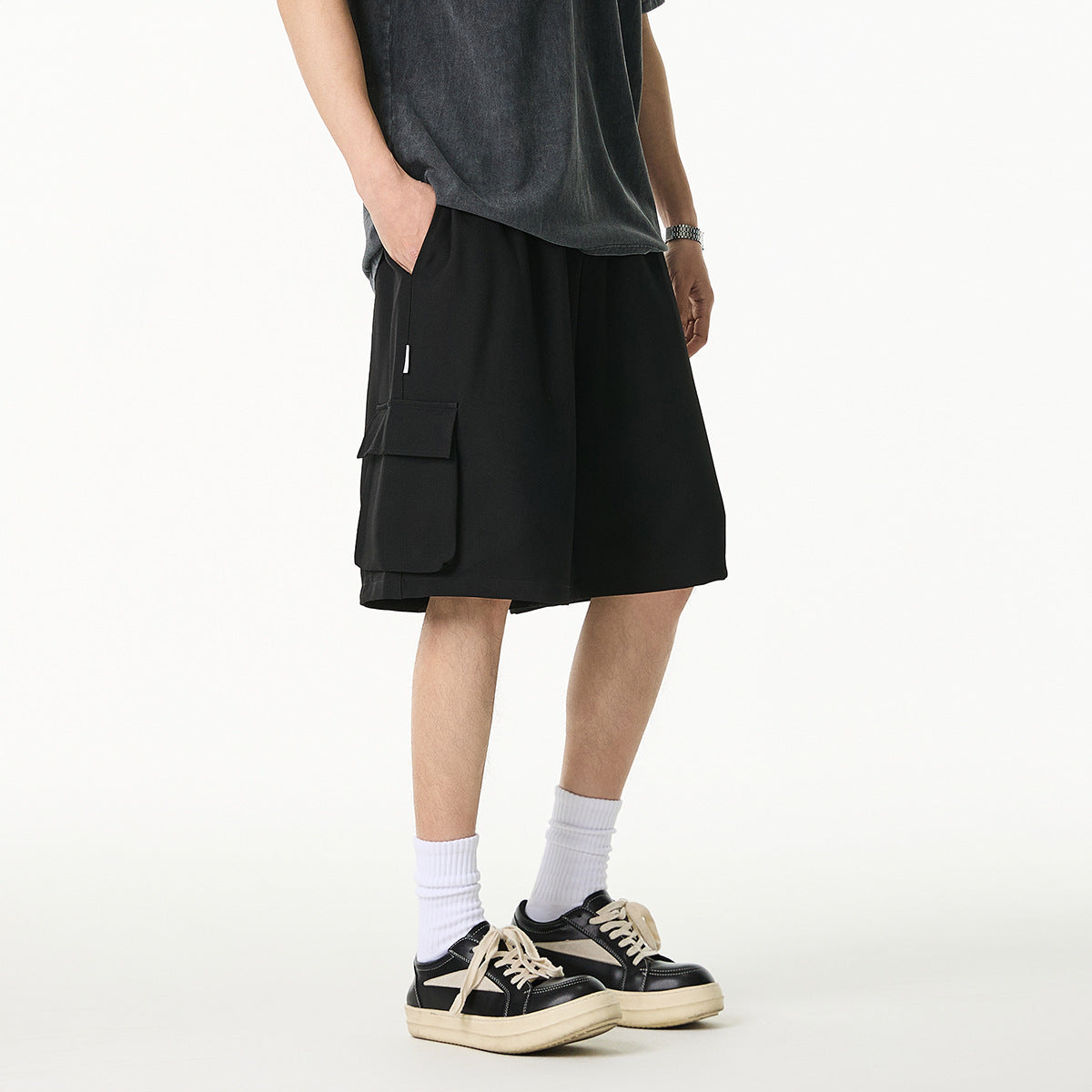 Model wearing loose black cargo shorts with large flap pockets, shown from a front-side angle.