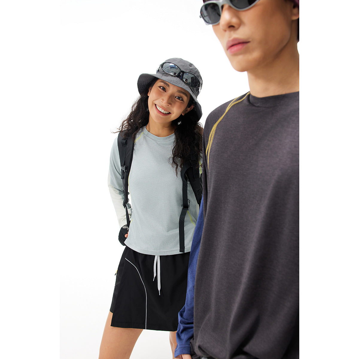 Two models in long-sleeve athletic tops: pale blue-gray on the woman and charcoal with yellow seam accents on the man.