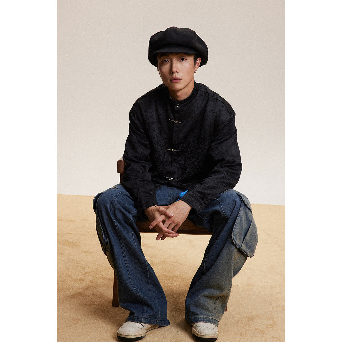 Model seated in a black stand-collar jacket with metal frog closures and subtle tonal bamboo embroidery.