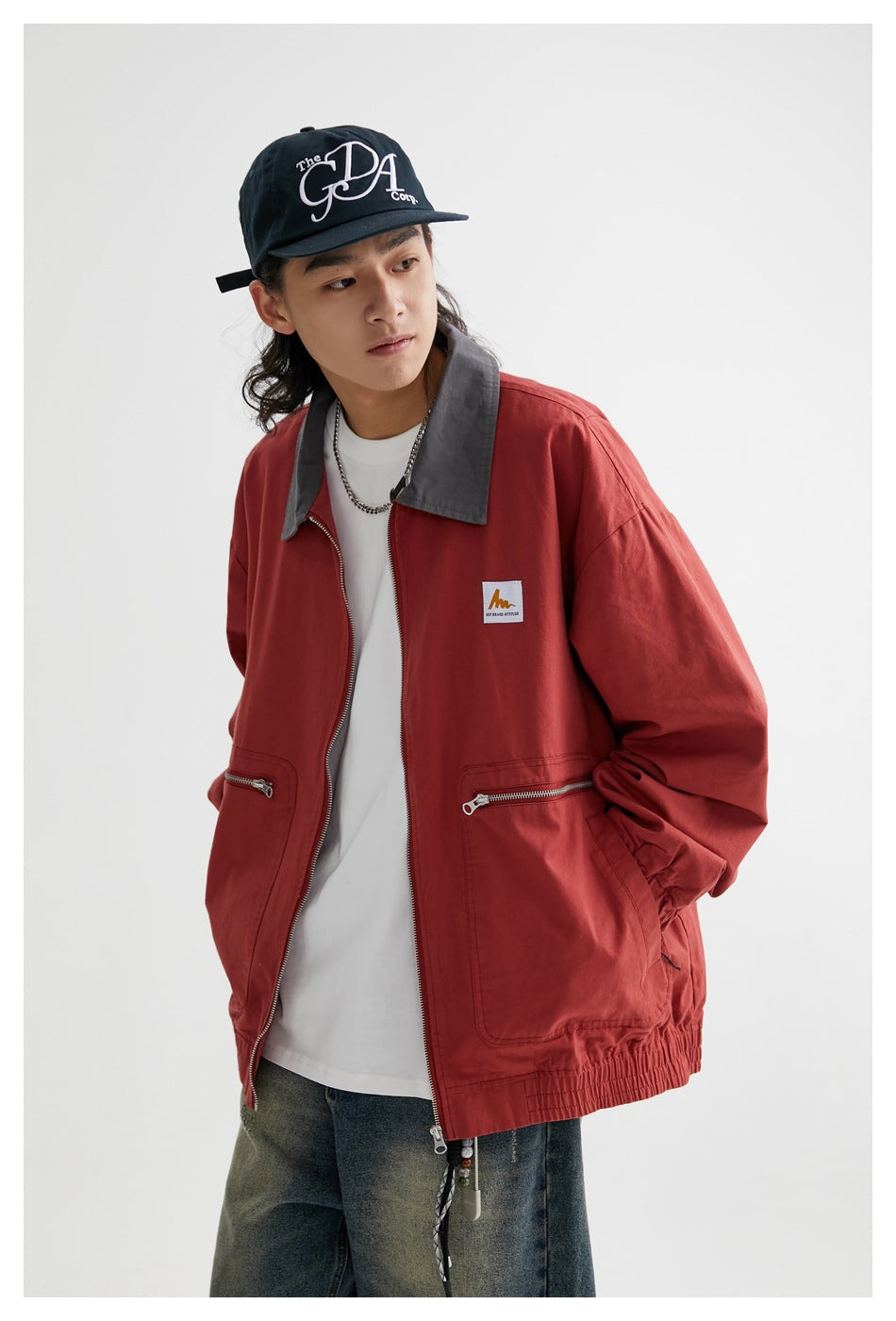 Model wearing a rust-red zip jacket with a gray collar, two zip pockets, and elastic cuffs and hem.
