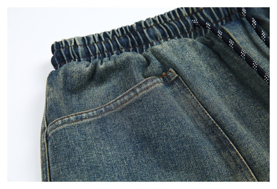 Close-up of faded blue denim shorts showing the gathered elastic waistband, black drawcord, and curved pocket stitching.