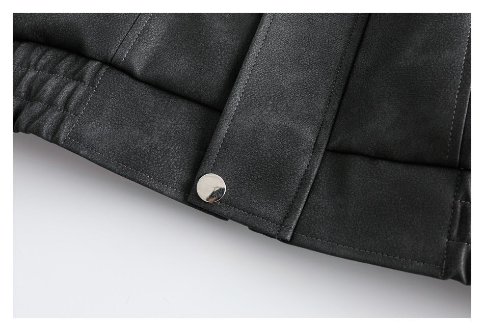 Close-up of a dark jacket hem with a metal snap, stitched placket, and gathered elastic section.