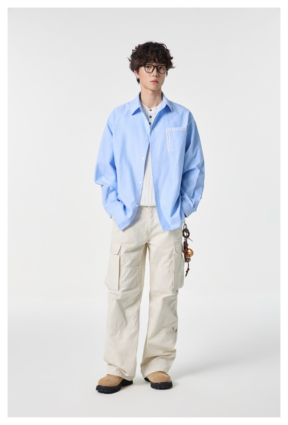 Model wearing a light blue button-up shirt with a plaid-trimmed chest pocket and cream cargo pants.