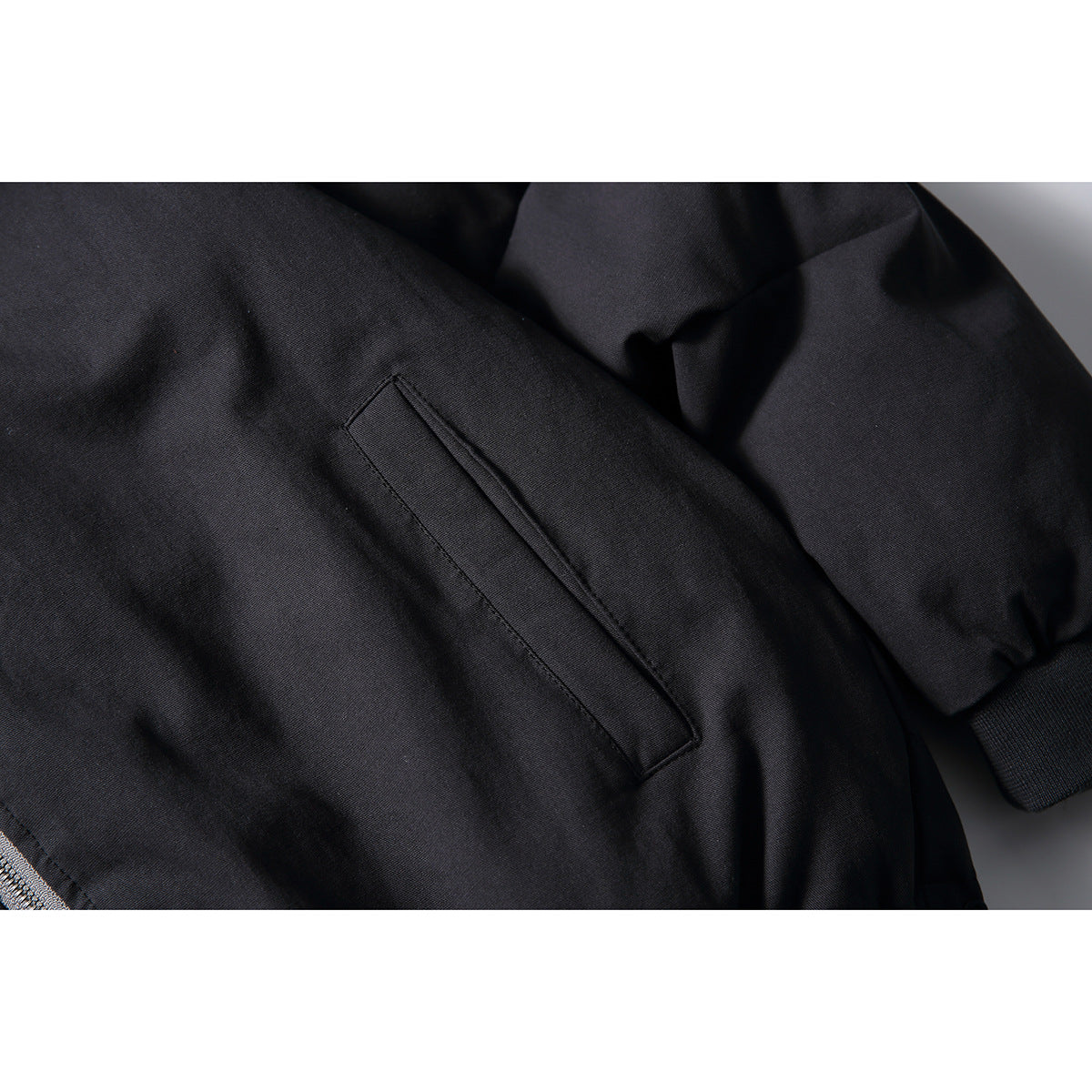 Close-up of a slanted welt pocket and ribbed cuff on the black jacket.