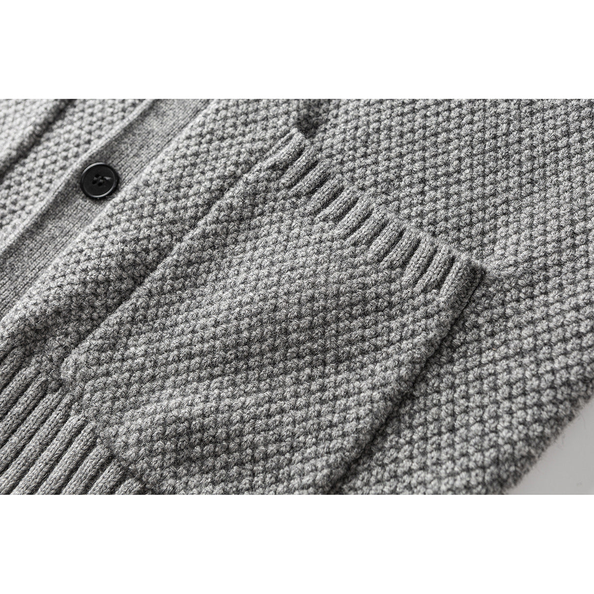 Close-up of a gray knit cardigan’s textured fabric, button placket, and front pocket.