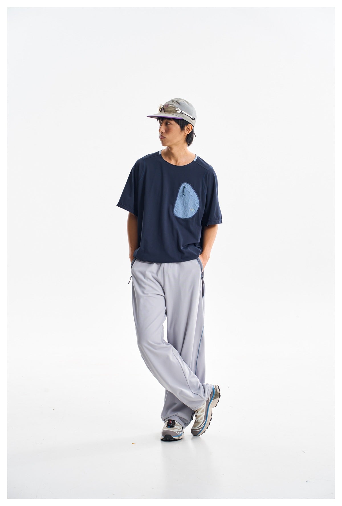 Model wearing a navy short-sleeve shirt with a light blue chest pocket and loose light gray pants.