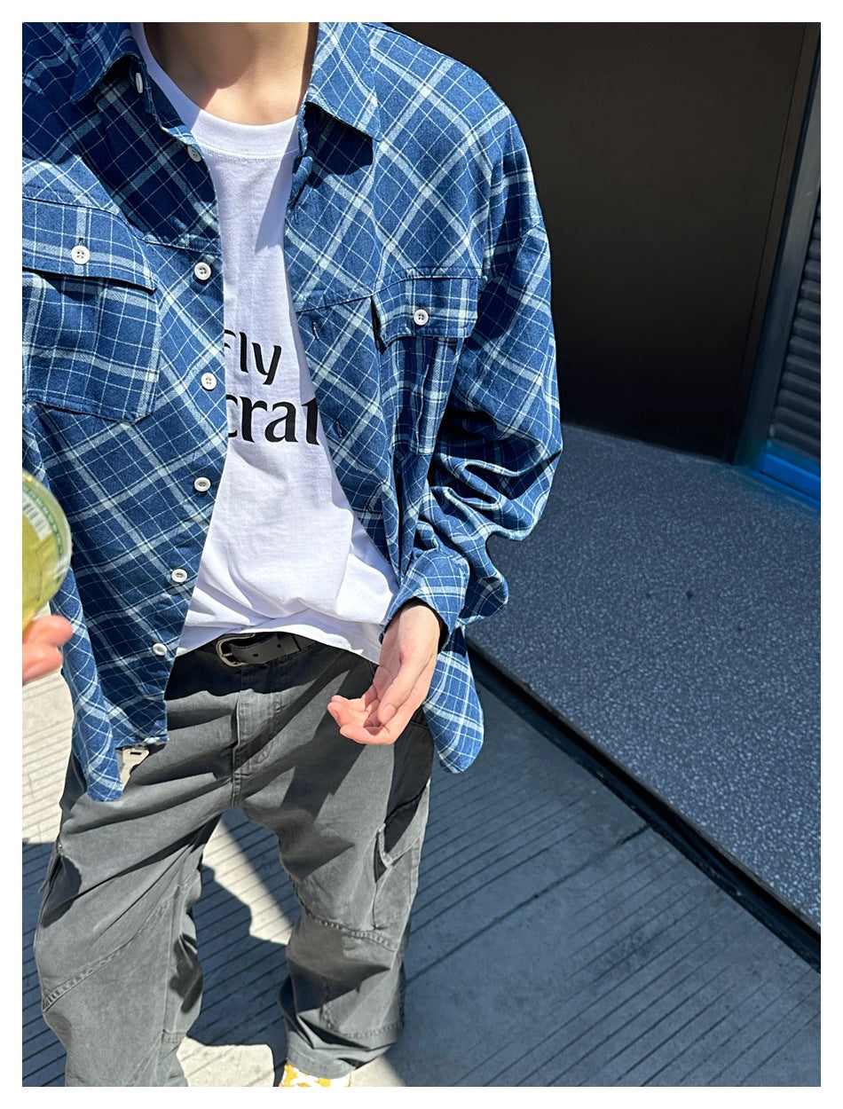 Close view of a person wearing an open blue-and-white plaid shirt with flap chest pockets over a white T-shirt.