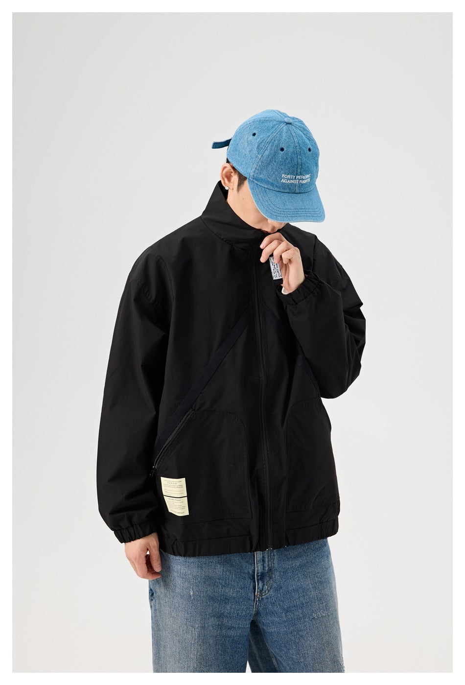 Close view of a model wearing a black zip jacket, highlighting the high collar, front pockets, and labels.