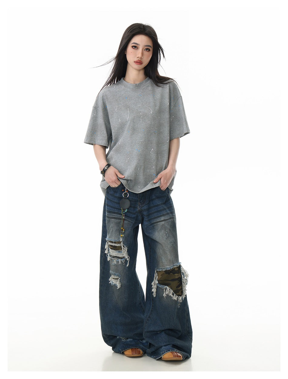 Front view of a model in an oversized gray speckled T-shirt and distressed, wide-leg dark blue jeans.