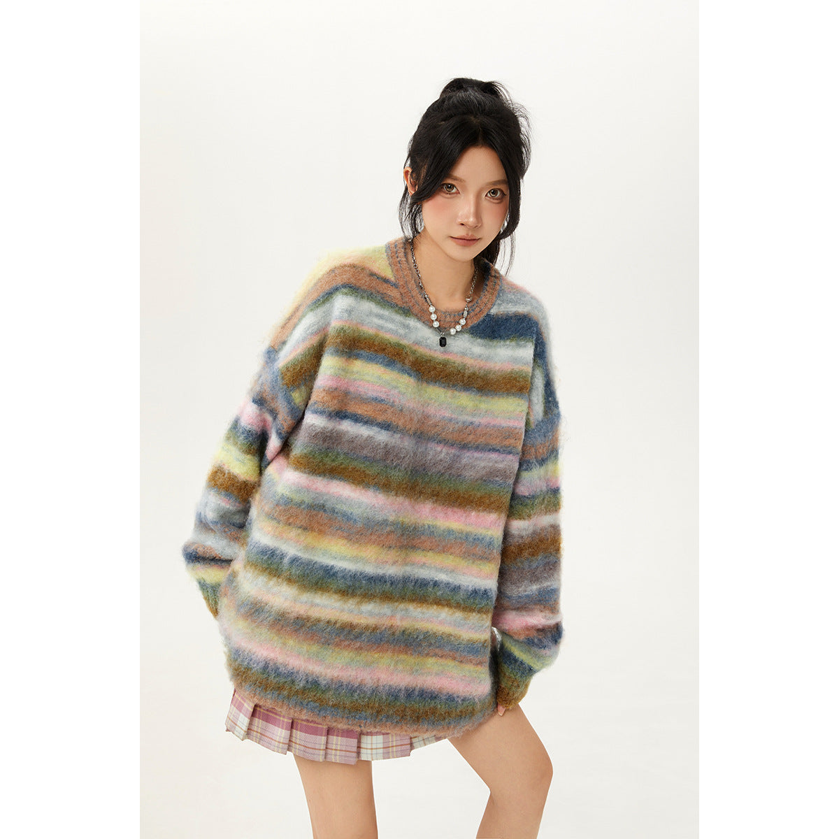 Closer front view of a model in an oversized fuzzy sweater with multicolor stripes and a pink plaid skirt.