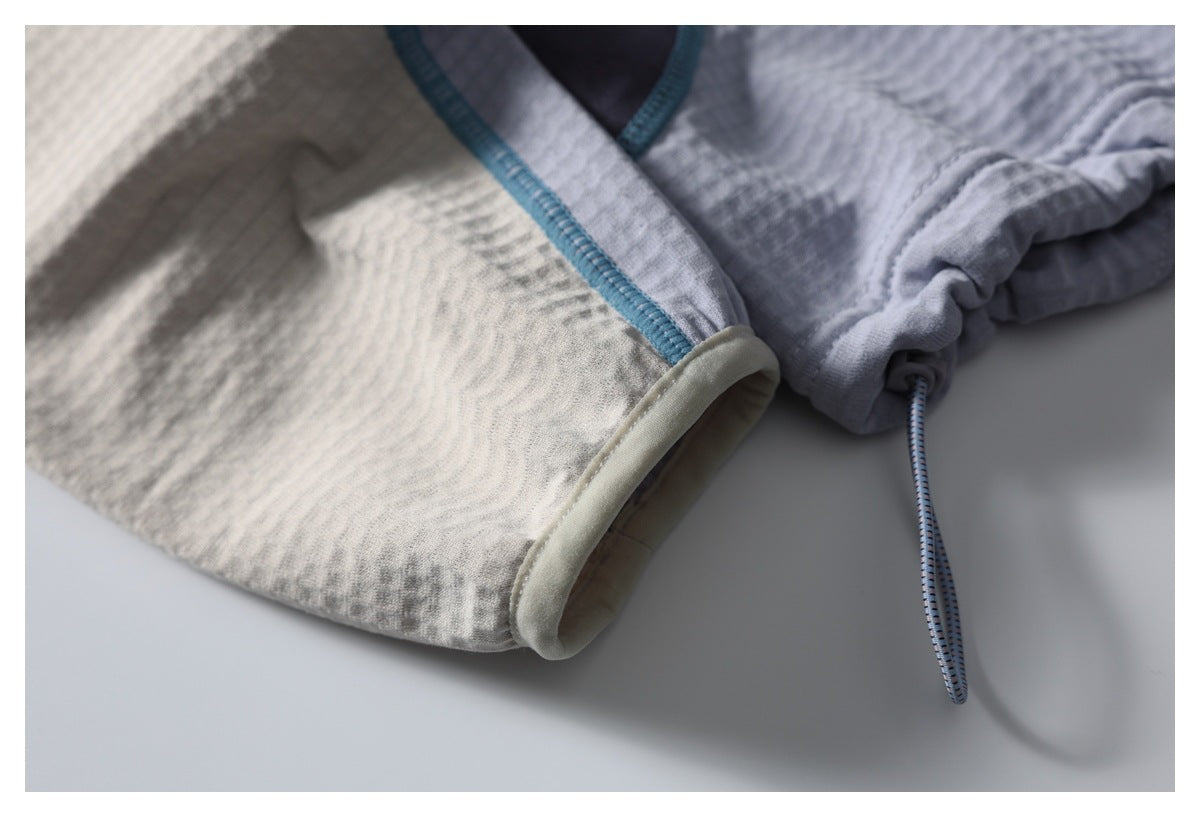 Close-up of a cream sleeve cuff and jacket hem with teal stitching and an adjustable drawcord.